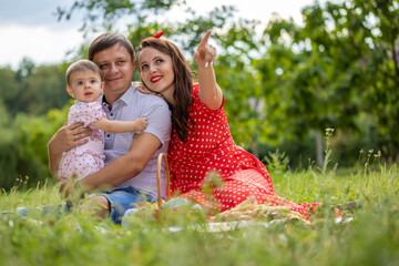 Happy young Family on the Walk in the Park. Mother, Father and Child Together the Joy on the Lawn and they have a Picnic. Concept Happiness of Family and Healthy Lifestyle.