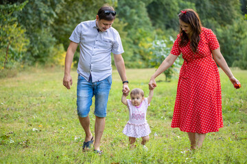 Happy young Family on the Walk in the Park. Mother, Father and Child Together the Joy on the Lawn and they have a Picnic. Concept Happiness of Family and Healthy Lifestyle.