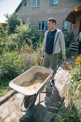 A man carries a garden wheelbarrow for loading sand to fill the paths