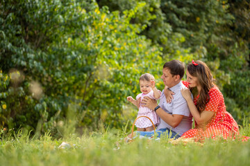 Fototapeta premium Happy young Family on the Walk in the Park. Mother, Father and Child Together the Joy on the Lawn and they have a Picnic. Concept Happiness of Family and Healthy Lifestyle.