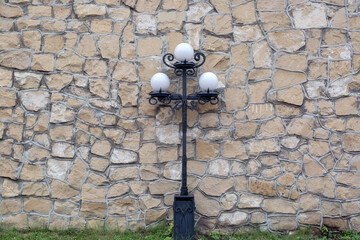 Beautiful black metal street lamp with three white balls on gray stone background. Copy space.