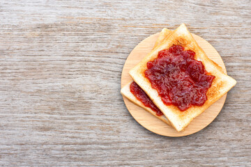 Toast sliced bread with red jam in wooden plate isolated on wooden table background. Top view. Flat...