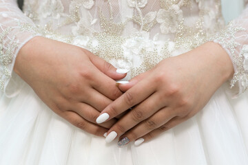 Obraz na płótnie Canvas Delicate hands of the bride with a white manicure on the background of the wedding dress.