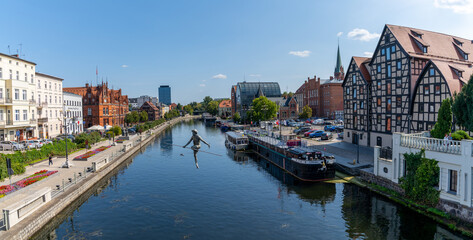 view of the historic waterfront warehouses and buildings on the Brda River in downtown Bygdoszcz with the Crossing the River sculpture in the foreground