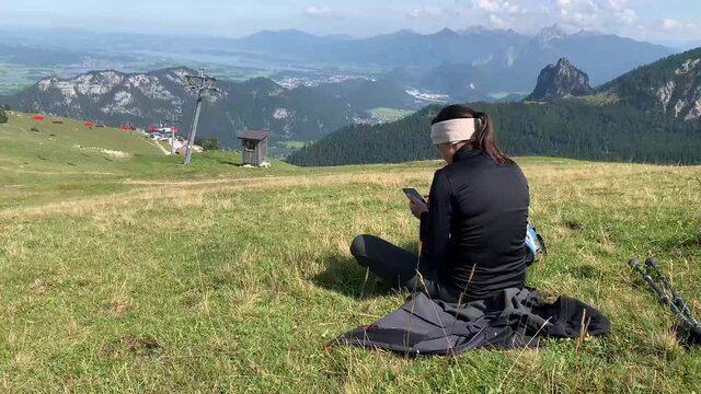Female hiker relaxing by taking a break in the Alps of Allg&auml;u Bavaria Germany with hiking ploes with mountain panorama in the background, Hochalp close to Pfronten