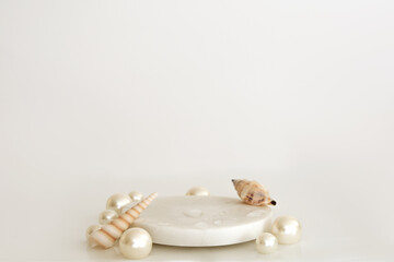 White marble podium with pearls, shells and water drops on the white background. Podium for product, cosmetic presentation. Creative mock up. Pedestal or platform for beauty products.