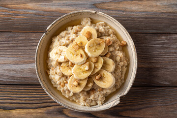 Oatmeal porridge in a bowl with banana, walnuts and honey on rustic wooden background. Top view. Healthy breakfast