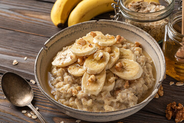 Oatmeal porridge in a bowl with banana, walnuts and honey on rustic wooden background. close up. Healthy breakfast
