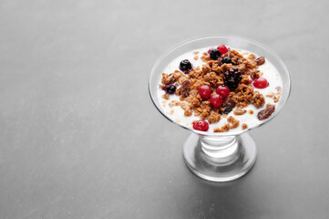 Cup of fresh yogurt with cereals and fruits over grey background
