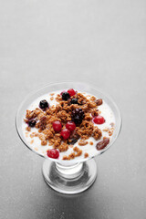Cup of fresh yogurt with cereals and fruits over grey background