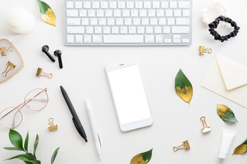Smartphone mockup with blank screen, computer keyboard and feminine accessories on white table. Flat lay, top view, overhead.