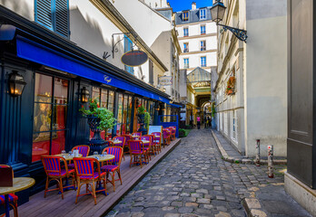 Narrow street with tables of cafe in Paris, France. Cozy cityscape of Paris. Architecture and landmarks of Paris.