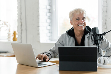 A radio host communicates with people. He speaks into the microphone about the news on the radio. An adult gray-haired man is working. A blogger's live show with the participation of listeners.