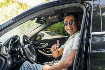Fototapeta na wymiar a young successful Asian businessman in sunglasses is sitting in an expensive modern car and smiling, looking at the camera