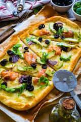 Pizza with smoked salmon, arugula, avocado, mozzarella and black olives on wooden background
