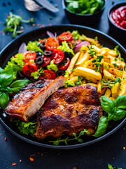 Tasty grilled ribs with french fries and fresh vegetables on wooden table

