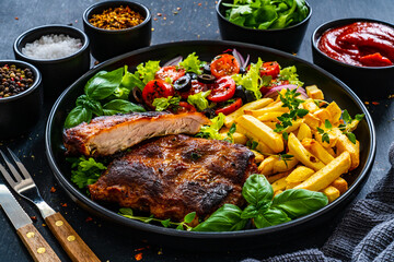 Tasty grilled ribs with french fries and fresh vegetables on wooden table
