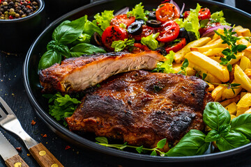 Tasty grilled ribs with french fries and fresh vegetables on wooden table
