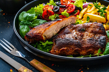 Tasty grilled ribs with french fries and fresh vegetables on wooden table
