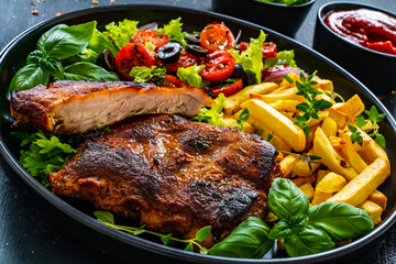 Tasty grilled ribs with french fries and fresh vegetables on wooden table
