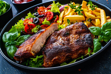 Tasty grilled ribs with french fries and fresh vegetables on wooden table
