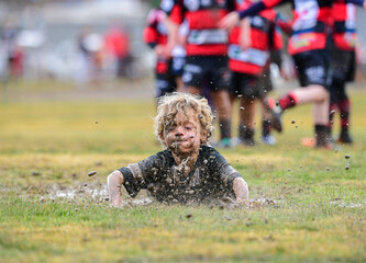 Junior rugby player belly slides in the mud
