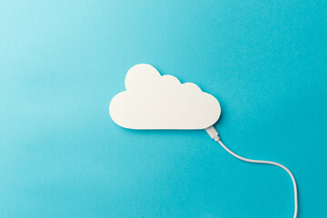 The concept of cloud technologies, cloud storage. A white cable is connected to a cloud on a blue background. Top view. Flat lay. Close-up. Copy space. Transferring data to cloud storage