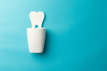 The concept of the International Day of the Dentist. A white cup for toothbrushes and a paper tooth on a blue background. Top view. Flat lay. Close-up. Copy space
