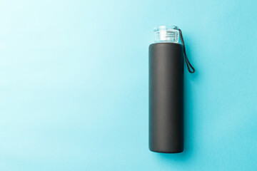 Stylish reusable eco-friendly glass bottle with a black rubberized surface on a blue background. Space for text. Top view. Flat lay. The concept of a lifestyle without plastic and waste