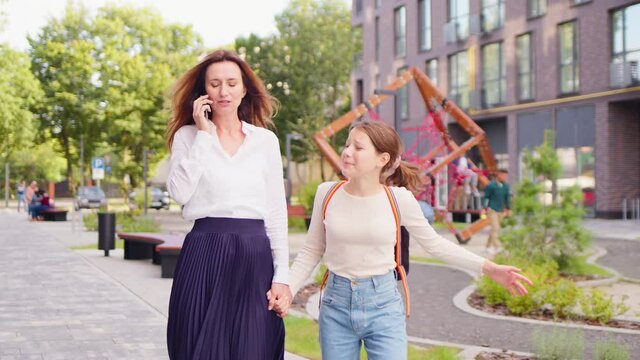 Young handsome mom take her daughter to school. Beautiful mother talk on telephone and pay no attention on girl.