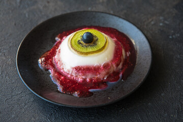Halloween dessert bloody eye from vanilla panna cotta and kiwi with berry syrup