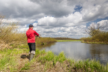 Fisher with a fishing rod stands on the river bank.