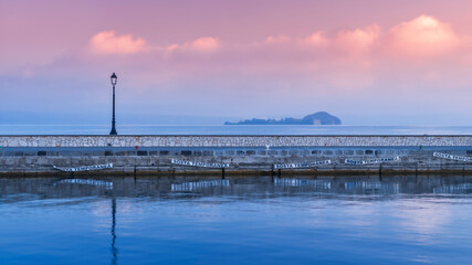 Fototapeta na wymiar panoramic view to pier with street lighter and view to island Bisentina at lake Bolsena in Italy