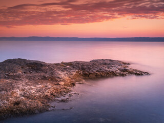 rock shore in sunrise twilight with smooth water and orange sky above lake Bolsena in Italy