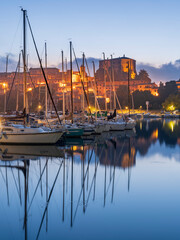 morning twilight and street lights around yachts with reflections in water in Capodimonte in Italy