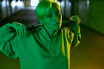 fashionable interesting shooting in the underground parking lot in neon colors. A girl with a short haircut holds a bat in her hands and looks straight into the camera. High quality photo