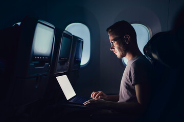 Man traveling by airplane. Young passenger using laptop during night flight.. © Chalabala