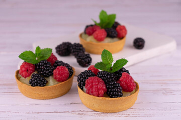 Berry tartlets with raspberries and blackberries and tender cream on a white wooden background.