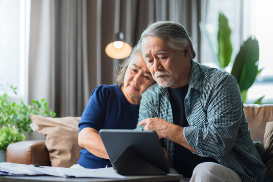 Serious stressed asian senior old couple worried about bills discuss unpaid bank debt paper, sad poor retired family looking at tablet counting loan payment worry about money problem