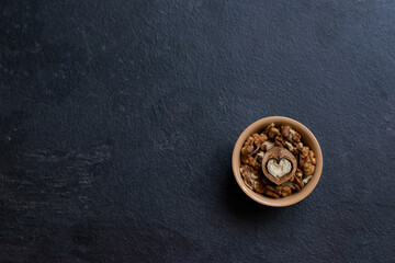 Walnut in a ceramic bowl on a dark background with copy space. View from above. In the center there is a half of a nut in the form of a heart. Ceramic plate with walnuts on a dark background. Place fo