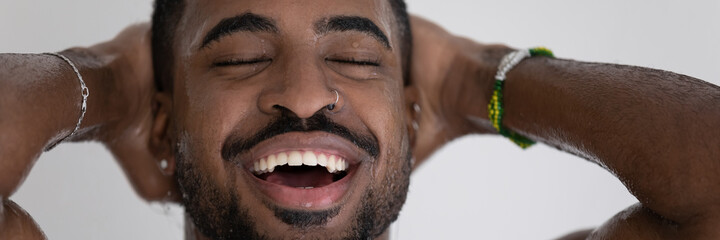 Wide panoramic photo happy African man with bracelets, piercing take a shower with eyes closed and hands behind head enjoy flowing water looking carefree, do morning routine. Skincare, hygiene concept