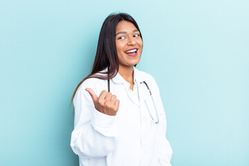 Young doctor Venezuelan woman isolated on blue background points with thumb finger away, laughing and carefree.