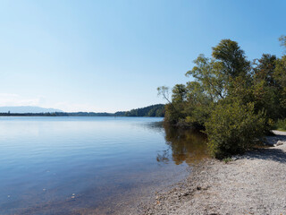 Kirchsee near Sachsenkam in Upper Bavaria, its moor lake amber and blue colored with popular small beach and bathing on wild shore