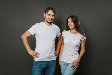 A young couple, a girl and a man in white blank t-shirts on a dark gray background. Mock-up. love story