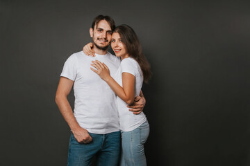 A young couple, a girl and a man in white blank t-shirts on a dark gray background. Mock-up. love story