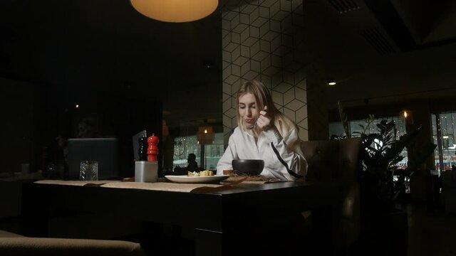 lonely blonde girl eating soup sitting in a restaurant against the backdrop of large windows and green plants. High quality FullHD footage