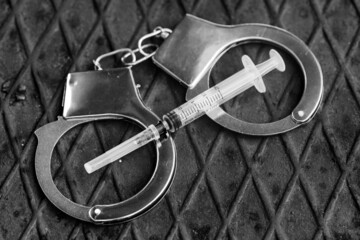 handcuffs with a syringe lie on a metal surface. drug-related crimes