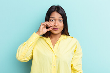 Young Venezuelan woman isolated on blue background with fingers on lips keeping a secret.