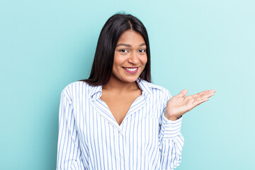 Young Venezuelan woman isolated on blue background showing a copy space on a palm and holding another hand on waist.