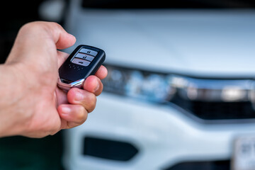 Hand of a man holding and push remote control of white car, technology transportation safety concept
